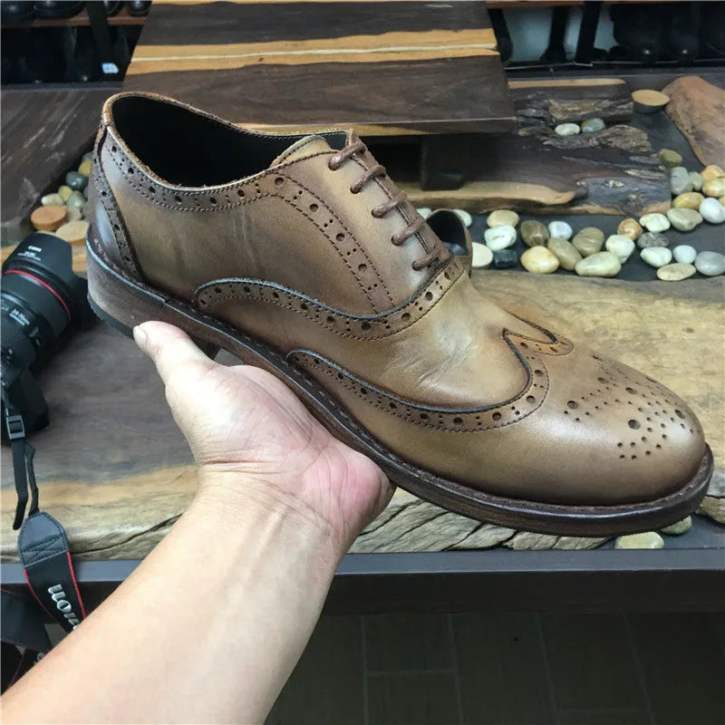 Men's light brown leather lace-up shoes with hand-carved distressed detailing on a wooden background.