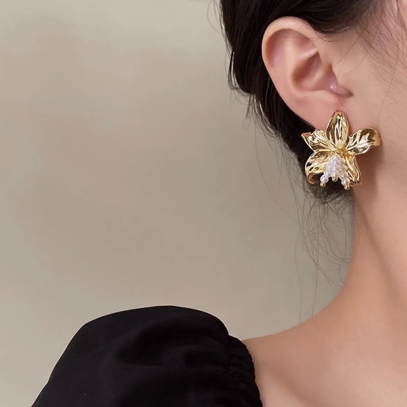 Golden flower-shaped earrings with pearl details on a white background.