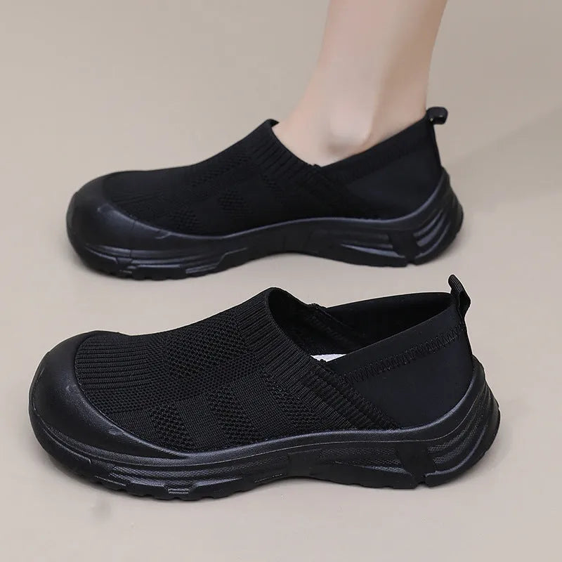 Women's black slip-on shoe cover with breathable cloth upper and flat PVC sole.