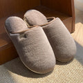 Pair of solid colour plush house slippers with a non-slip PVC sole, shown in coffee brown.