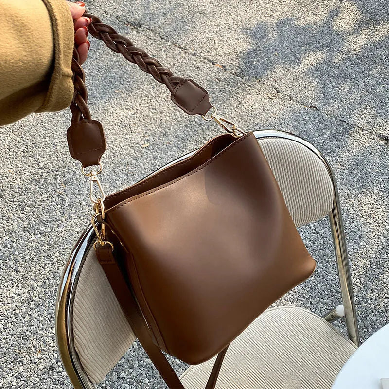 Retro style khaki woven PU leather crossbody bucket bag with an adjustable strap, shown in a casual setting.