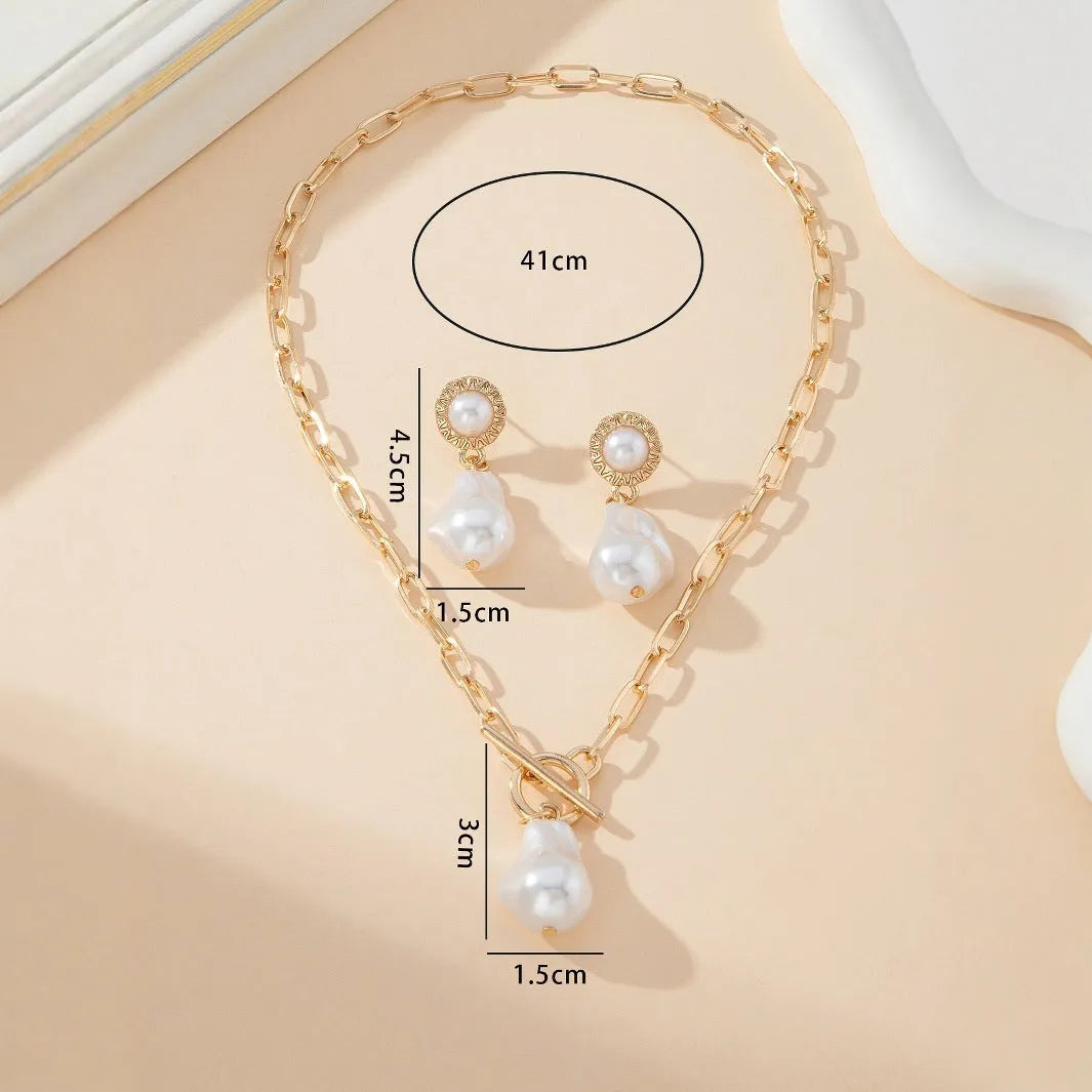 Gold-toned baroque pearl pendant necklace and matching stud earrings set on a dark background.