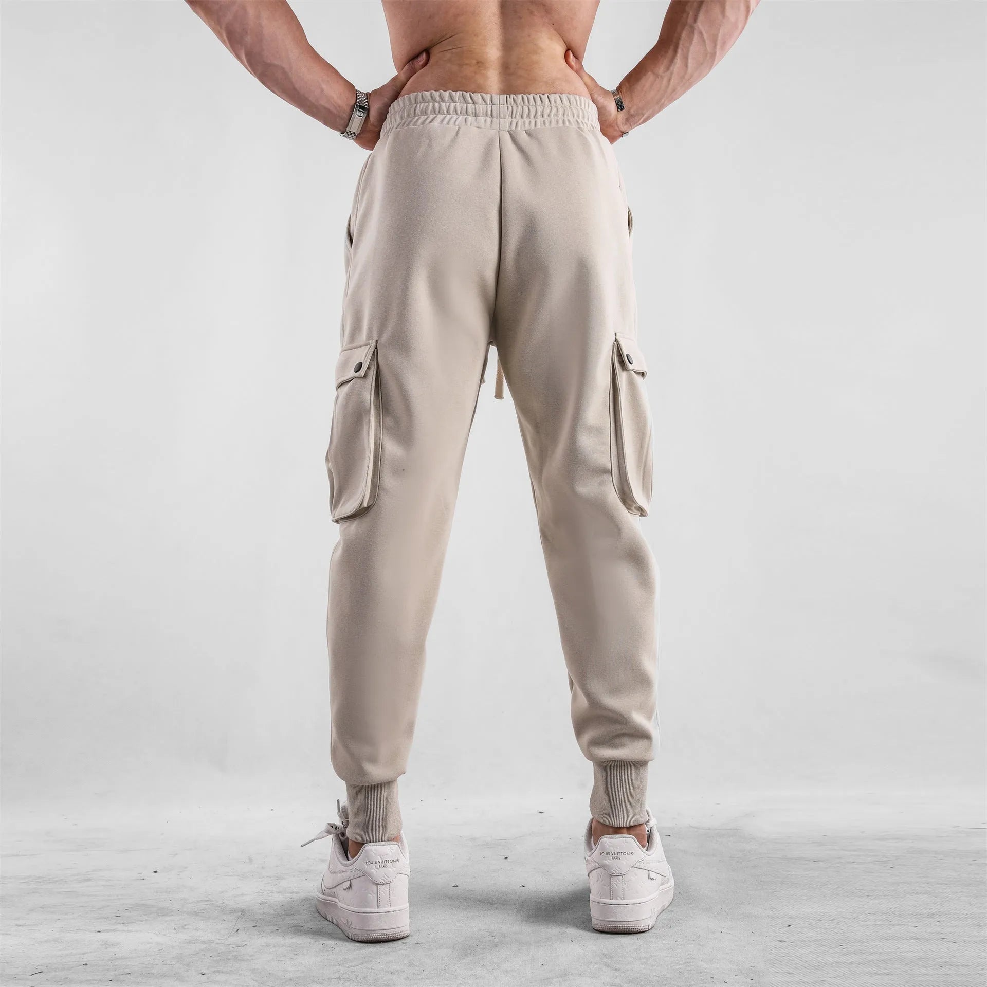 Men's loose-fit beige cotton trousers with tied ankle cuffs and multiple pockets on a neutral background.