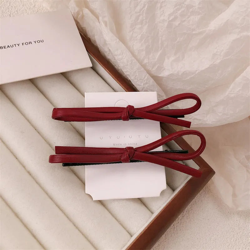 Wine red genuine leather bow hair barrette with metal clip on a white background.