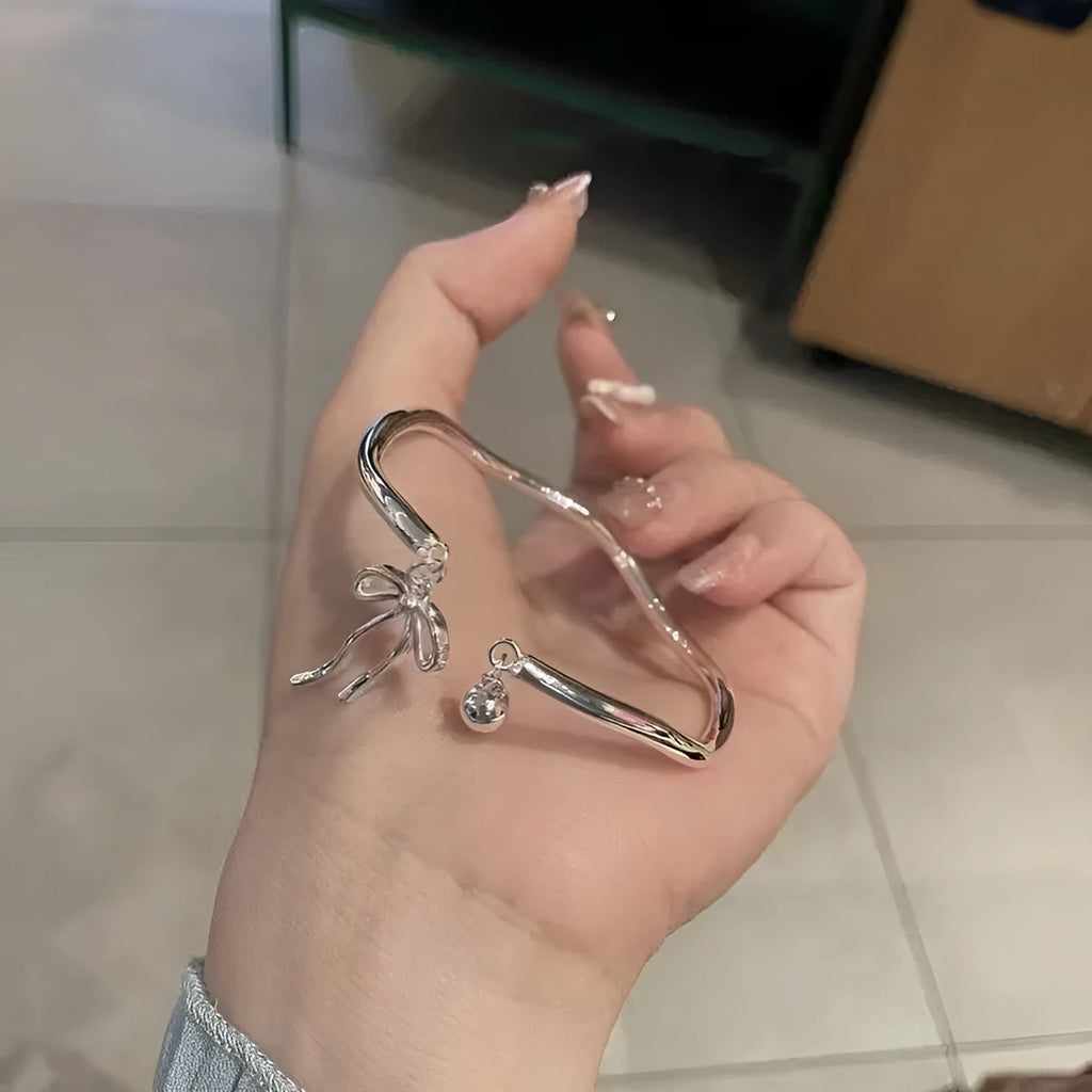 Silver toned adjustable bracelet with bow bell charm on a wrist, showing lobster clasp.