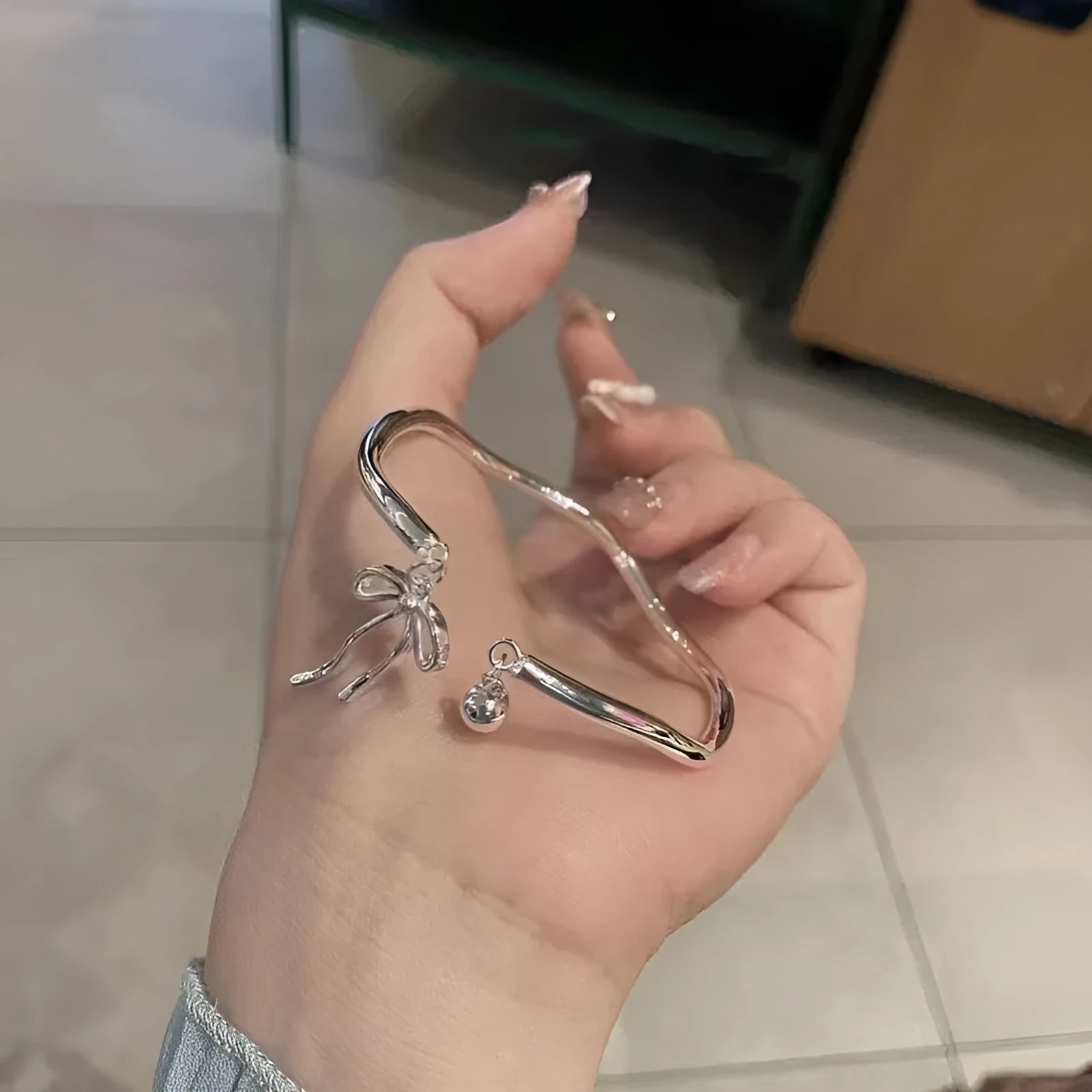 Silver toned adjustable bracelet with bow bell charm on a wrist, showing lobster clasp.