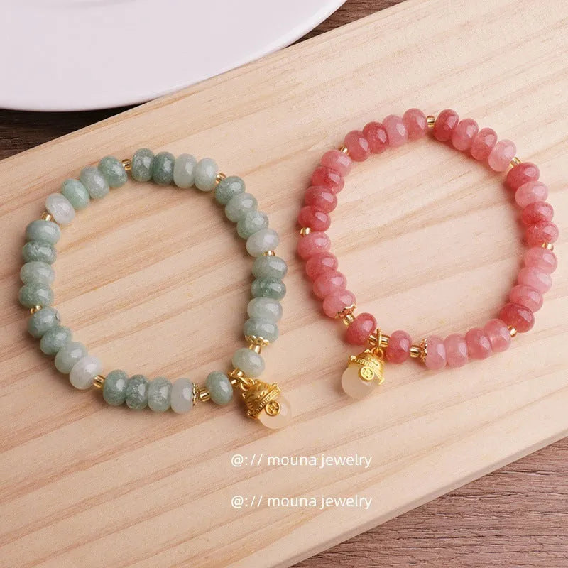 Women's strawberry quartz bracelet with lucky cat charm on grey background