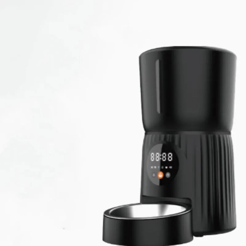 Black automatic pet feeder with digital display and food hopper on a wooden floor.