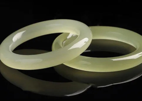 A polished natural jade round bar bracelet showing a winding silk texture on its surface.