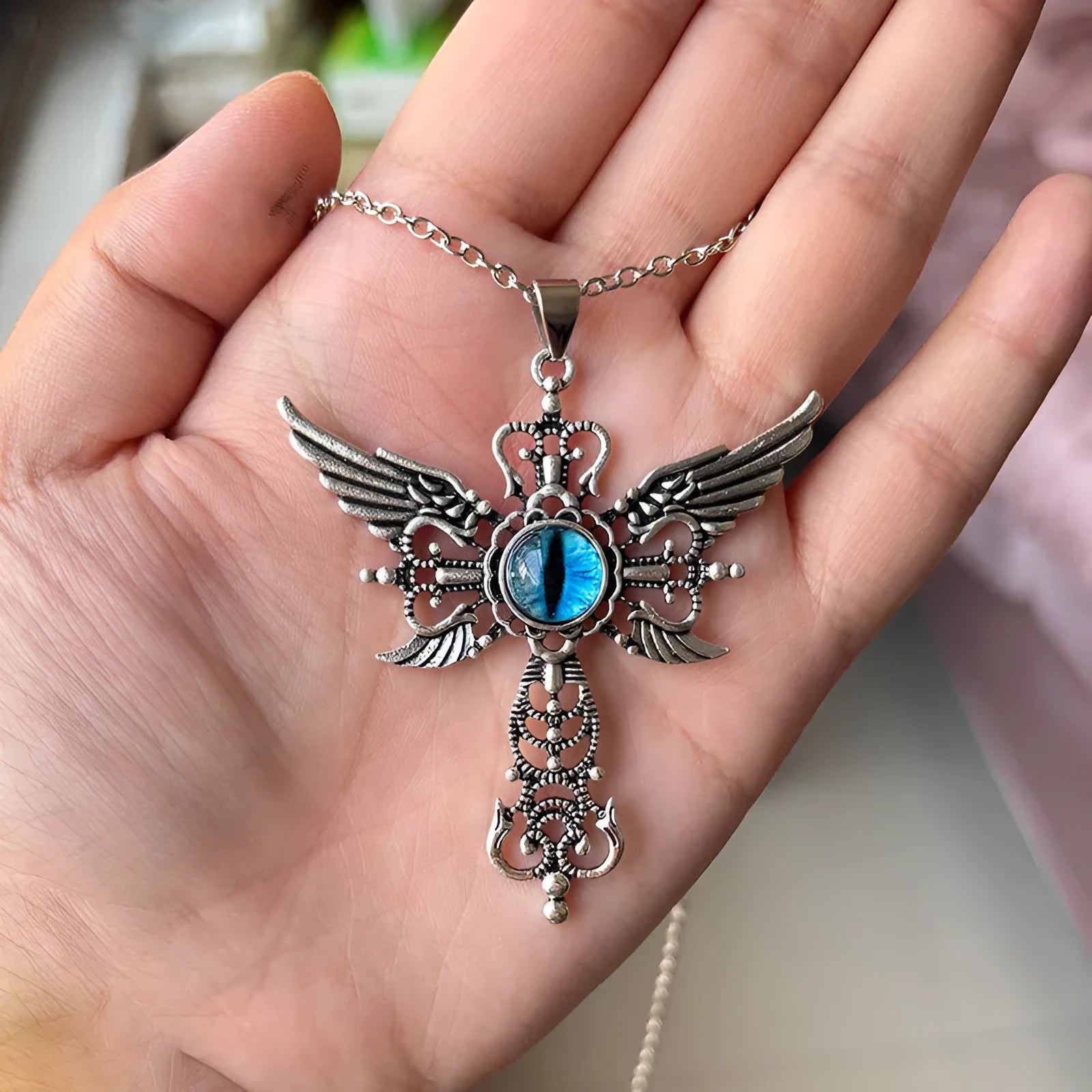 Close-up of a silver-coloured geometric pendant with wing details and a central cross on a chain.