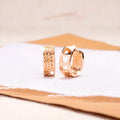 A pair of circular rose gold tone earrings featuring a hollowed-out heart shape design on a white background.