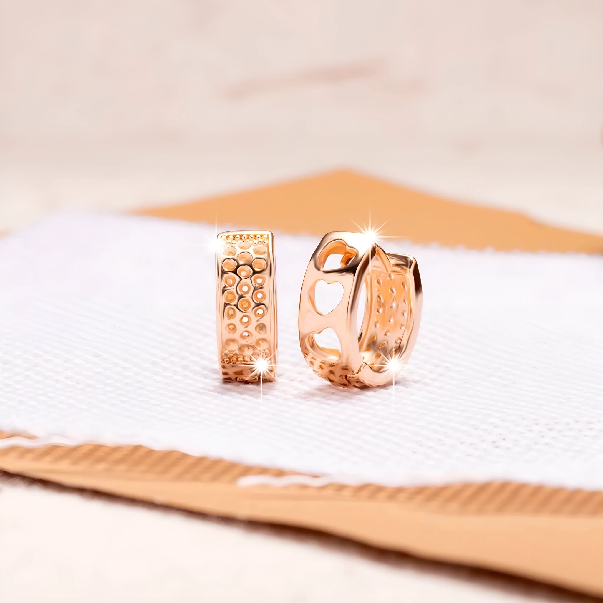 A pair of circular rose gold tone earrings featuring a hollowed-out heart shape design on a white background.