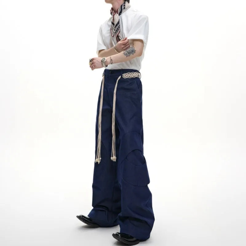 Men's dark blue straight-leg jeans showing loose fit, belt stitching with tassel, and zip pocket decorations.