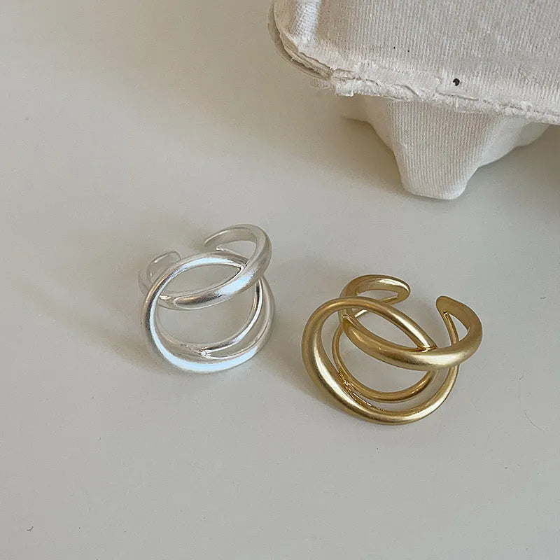 Geometric open ring with interlaced metal design and matte finish in gold colour.
