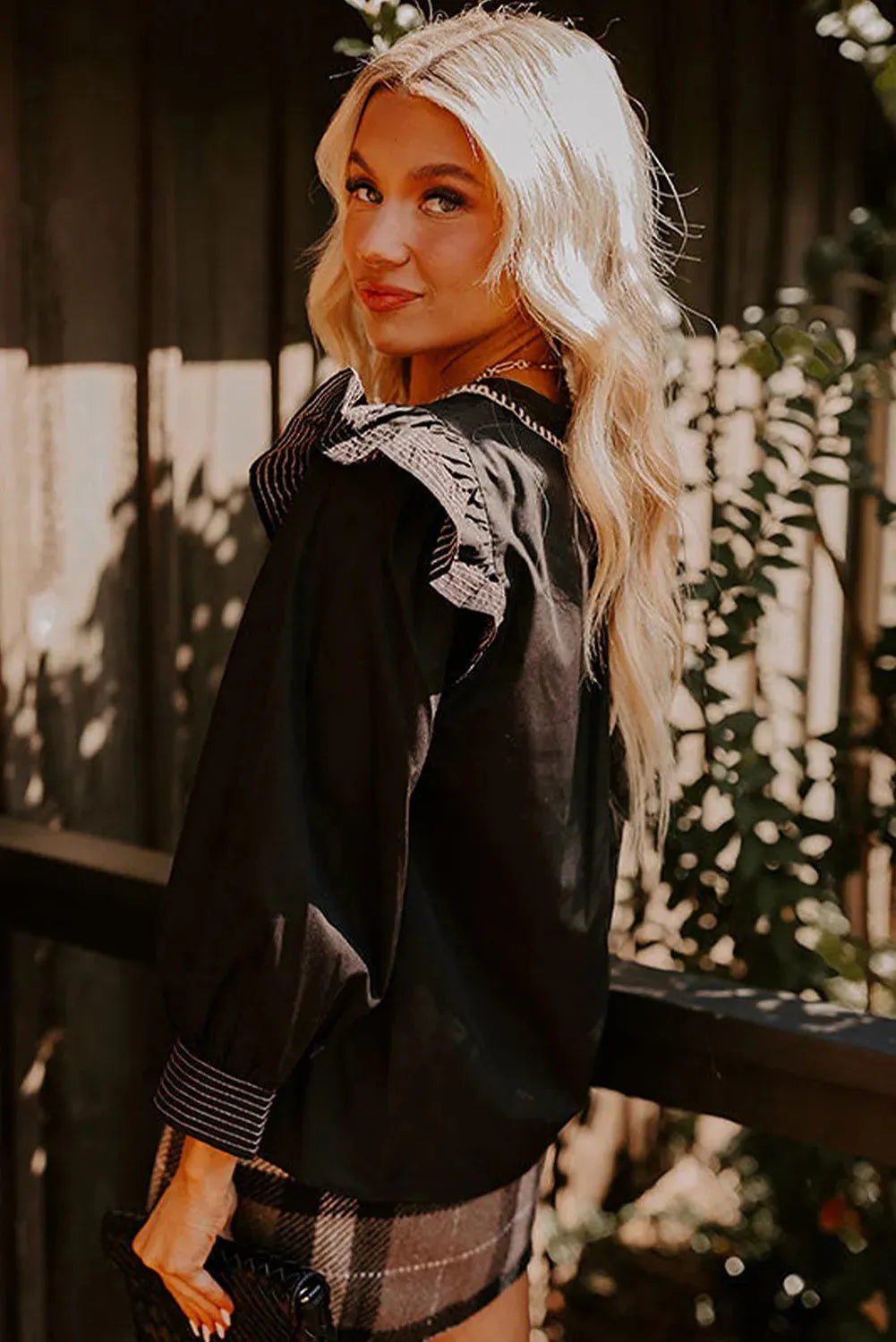Black long sleeve women's blouse with V-neck, contrast stitching, and ruffle sleeve details.