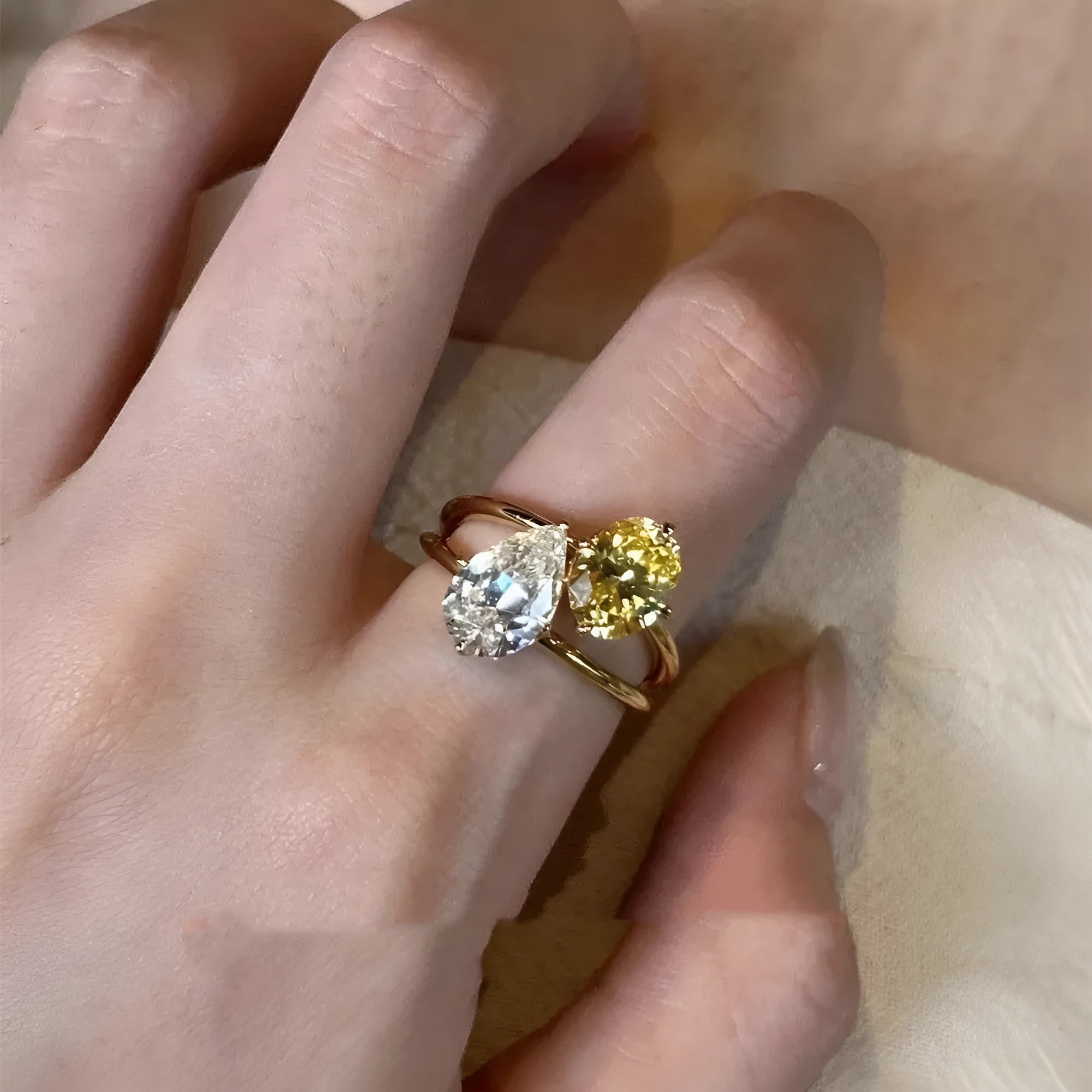 Geometric open-back silver ring with large central pear-cut clear zircon stone on a model's hand.