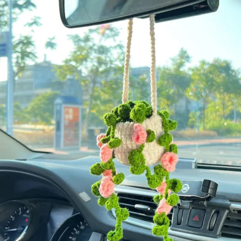 Green and white crocheted wool car plant decoration with a white hanging rope.