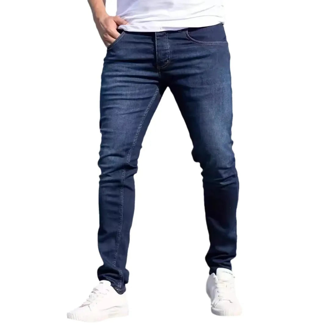 Men's dark blue slim-fit skinny jeans with a zip fly and mid-rise waist on a plain background.