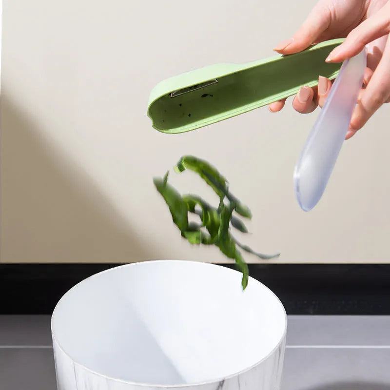 Dark green kitchen peeler with plastic handle inside its clear storage tube on a wooden surface.