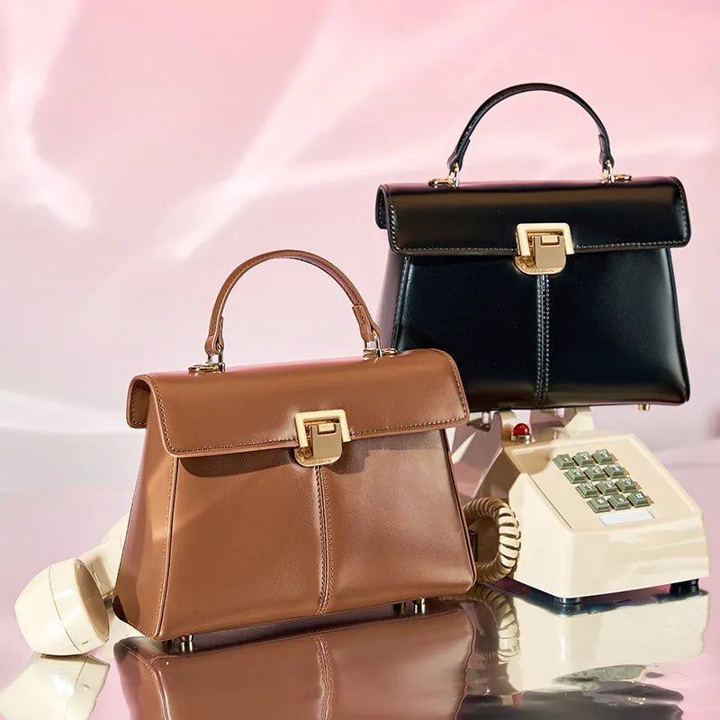 Women's black genuine leather shoulder bag with a clasp, shown with adjustable strap and open to reveal internal zippered pocket.
