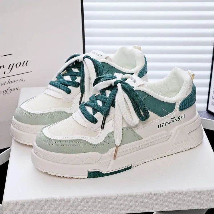Beige children's platform trainers with cross shoulder straps and white rubber soles on a wooden floor.