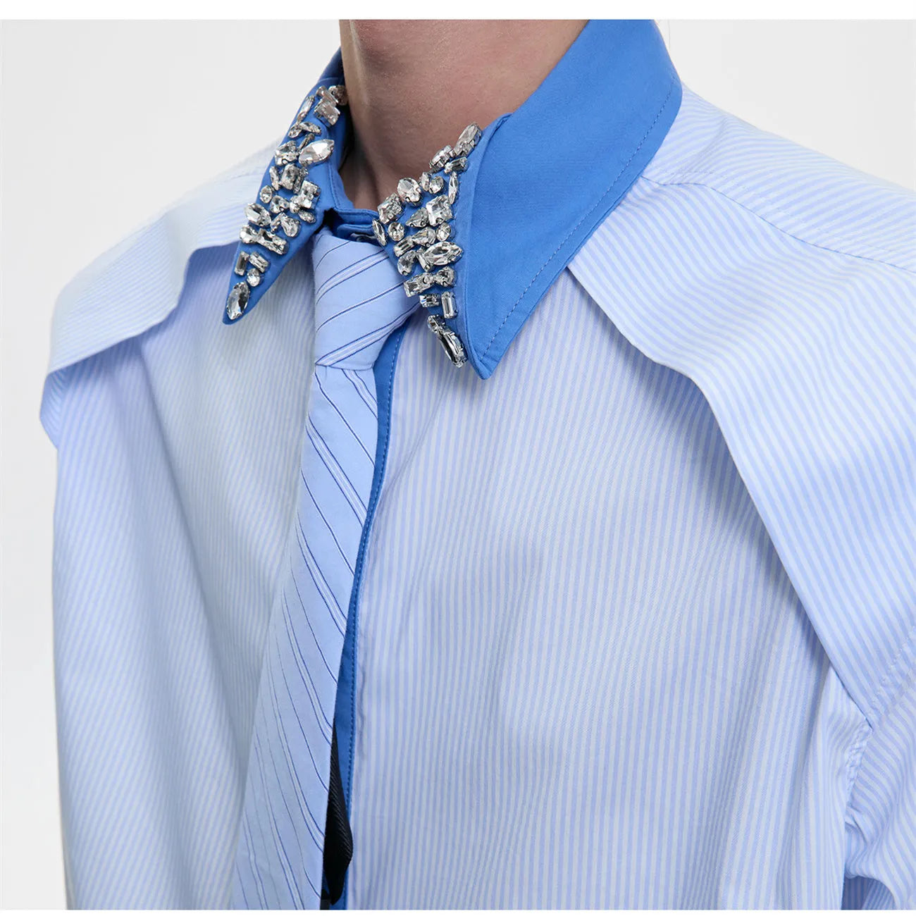 Man wearing a blue loose fit shirt with patchwork stripes, a diamond tie detail, and a flip collar.