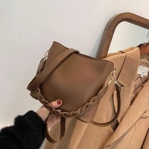 Retro style khaki woven PU leather crossbody bucket bag with an adjustable strap, shown in a casual setting.