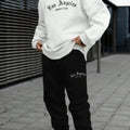 Man wearing a grey hooded pullover sweater and matching tracksuit bottoms from a winter sports leisure set.