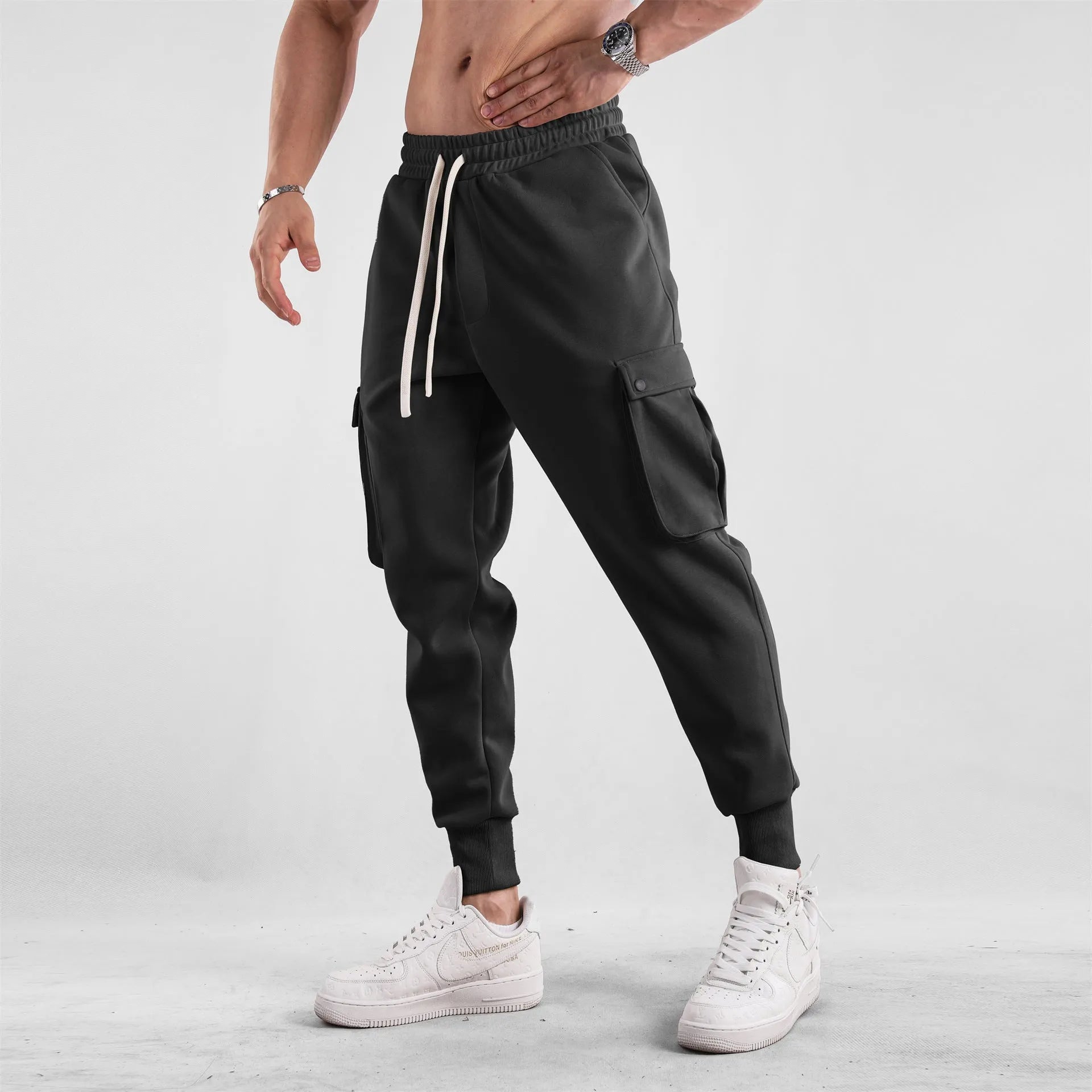 Men's loose-fit beige cotton trousers with tied ankle cuffs and multiple pockets on a neutral background.
