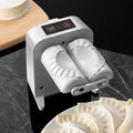 White automatic electric dumpling maker machine with USB cable, brush, and spoon on a kitchen counter.