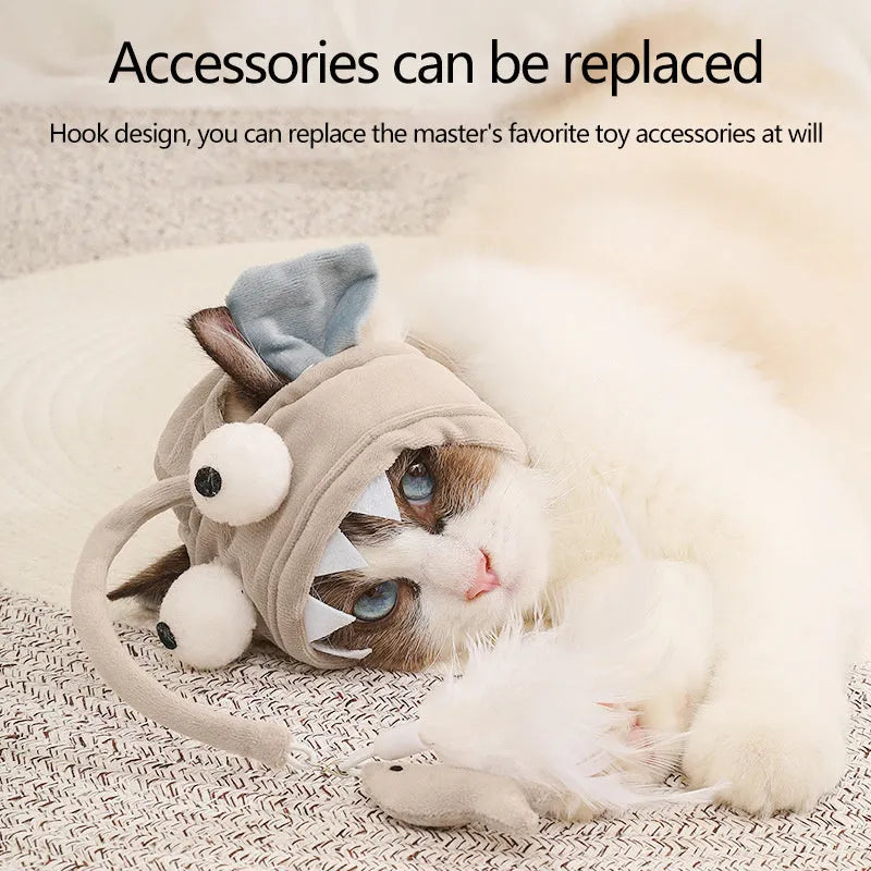 Grey dinosaur-themed cat headband toy with big eyes, a feather teaser, and an adjustable strap for hands-free play.