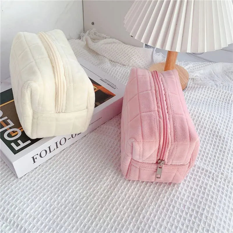 Three plush makeup bags in pink, white, and blue with zippers, laid flat showing front