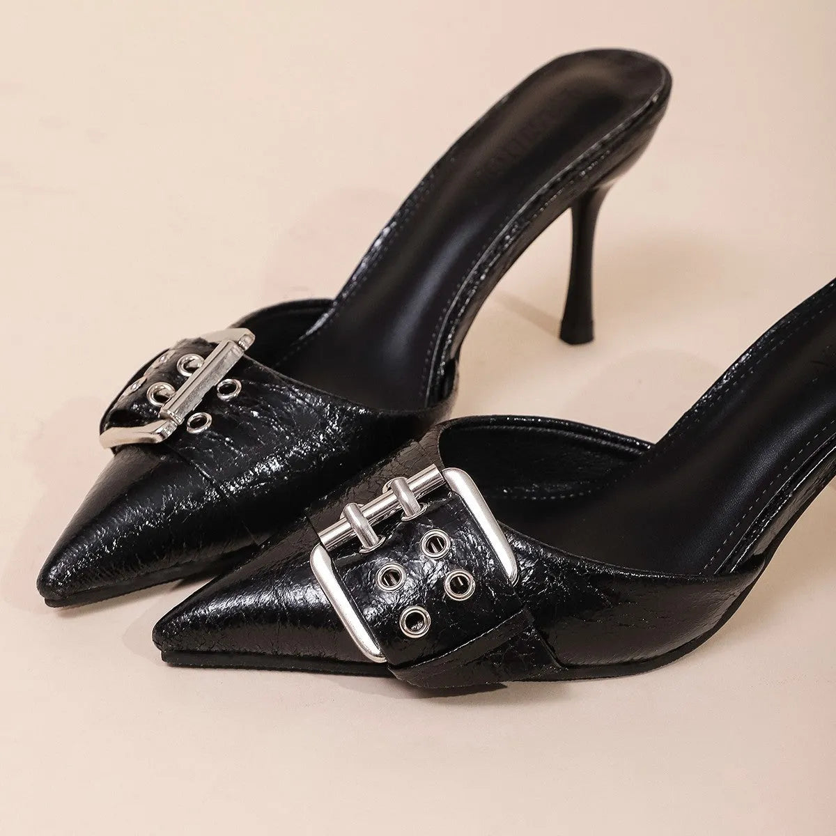 Black women's high heels with pointed toe and buckle decoration on ankle strap.