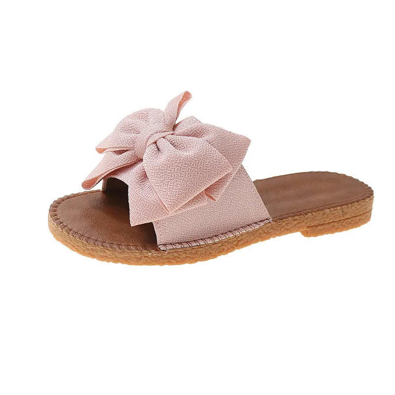 Women's beige suede slip-on sandals with a bow detail and soft rubber sole.