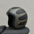 Retro-style half motorcycle helmet in fibreglass, shown in Cement Grey colour on a stand.