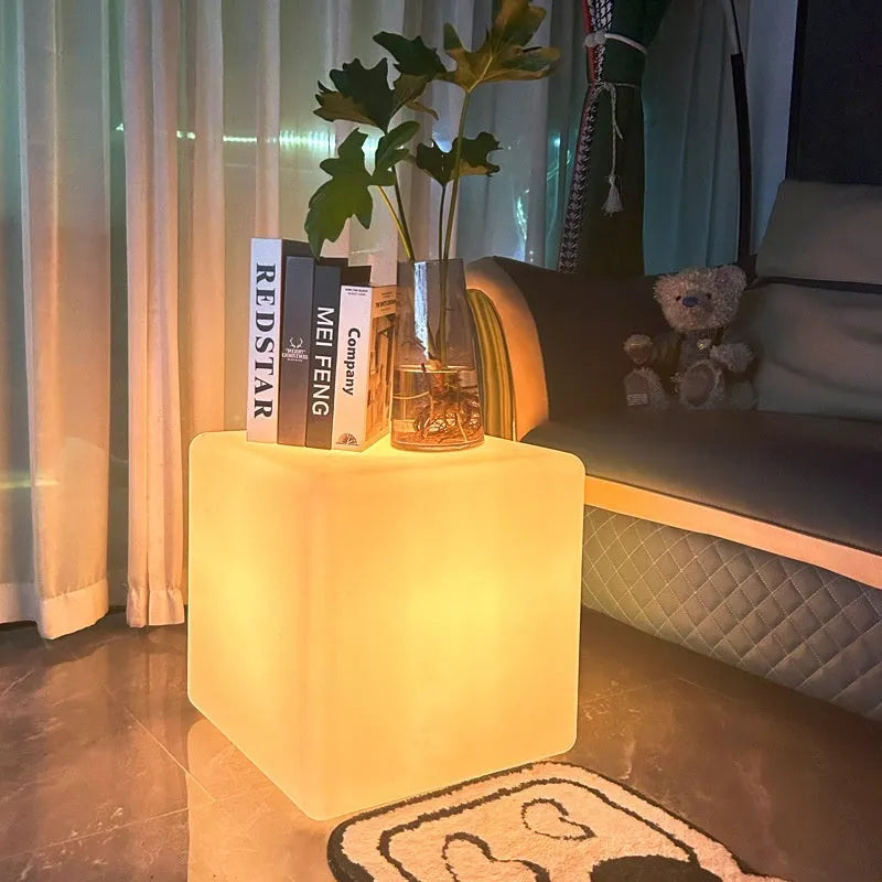 A modern square white LED cube light stool in a garden setting, showing its size options.