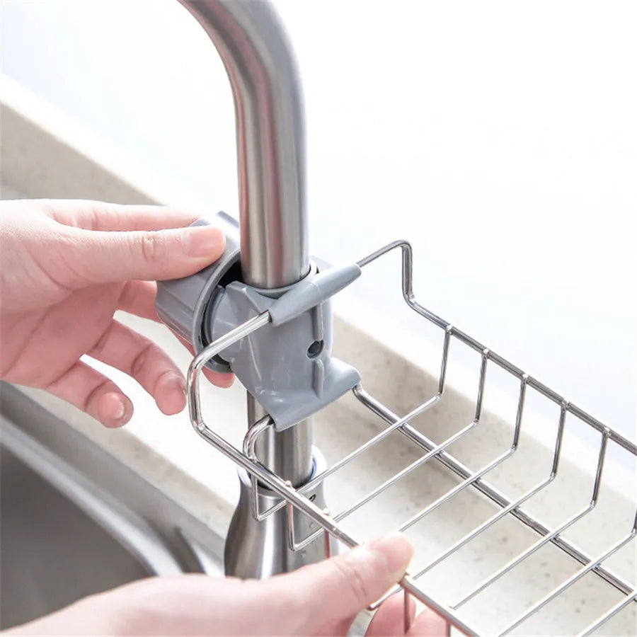 Adjustable stainless steel sink drain rack clipped onto a kitchen faucet with sponge and soap stored on the removable holder