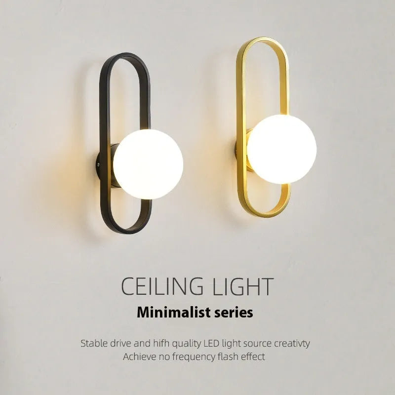Minimalist circular wall lamp with glass shade on iron arm, in black finish, mounted beside a bed.