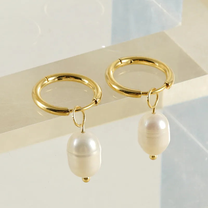A pair of gold geometric drop earrings featuring stainless steel construction and central freshwater pearls.