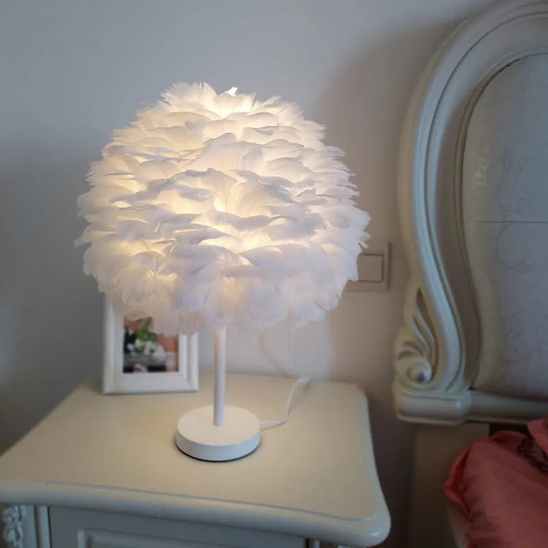 Handmade feather table lamp with metal base, white feathers, and remote control on a wooden bedside table