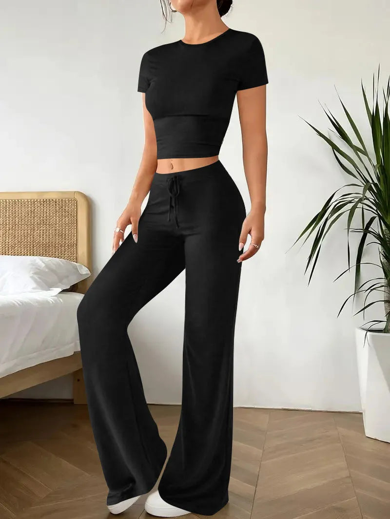 A woman's black high-waist trousers and matching short-sleeve T-shirt co-ord set laid flat.