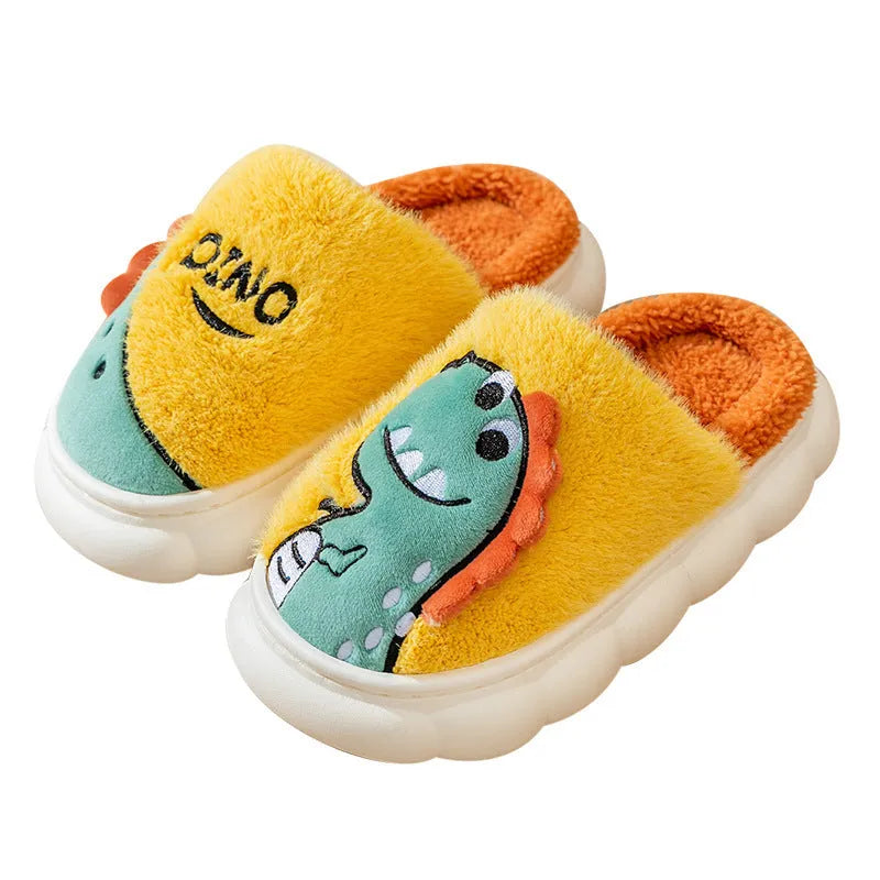A pair of grey dinosaur-print plush slippers on a wooden floor, showing the soft cotton upper and thick textured sole.