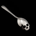 Stainless steel skull-shaped coffee spoon with polished finish on a flat surface