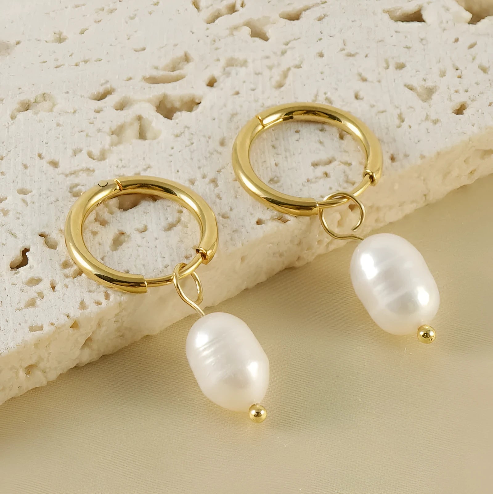 A pair of gold geometric drop earrings featuring stainless steel construction and central freshwater pearls.