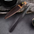 Black stainless steel hand pry tea knife on dark surface with tea leaves