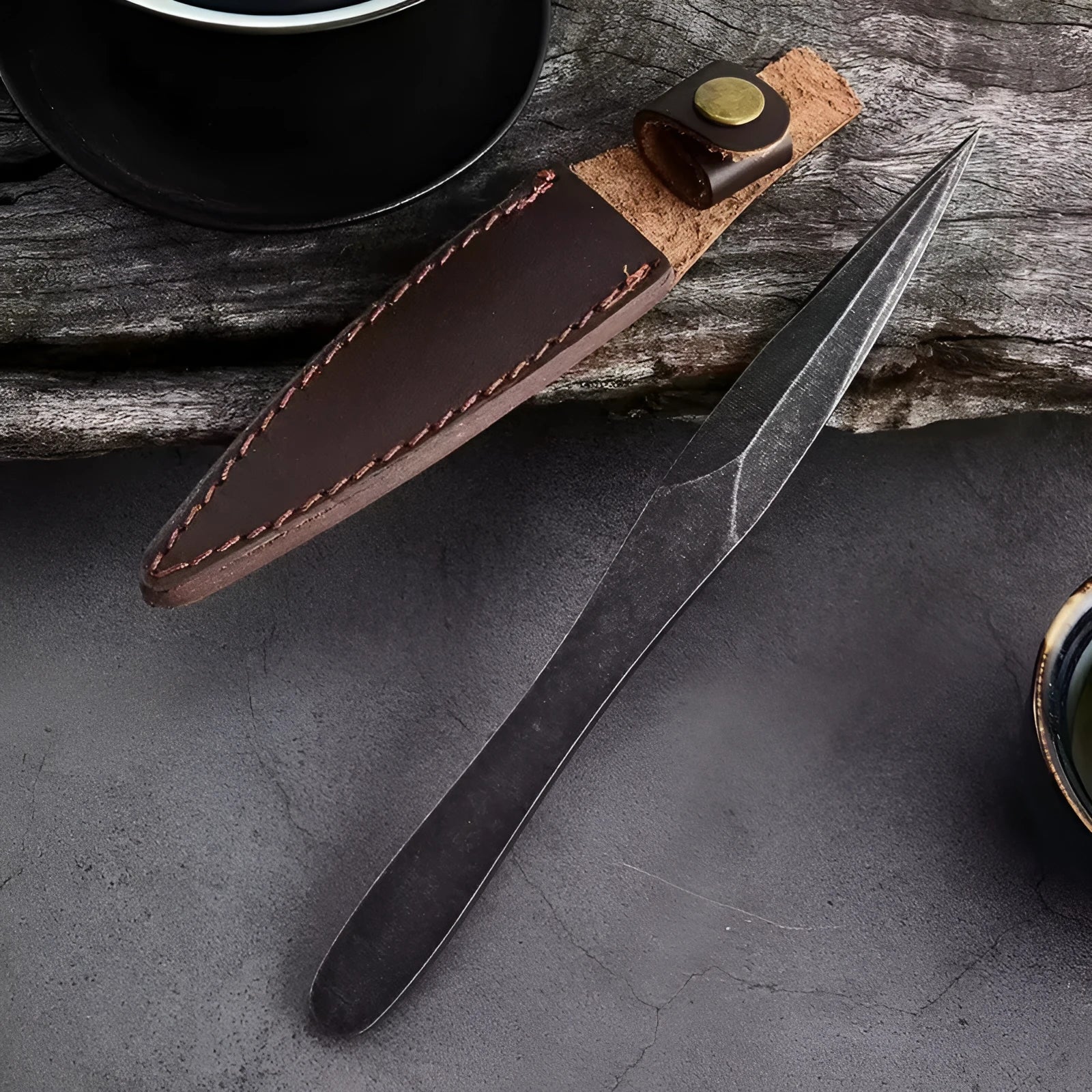Black stainless steel hand pry tea knife on dark surface with tea leaves