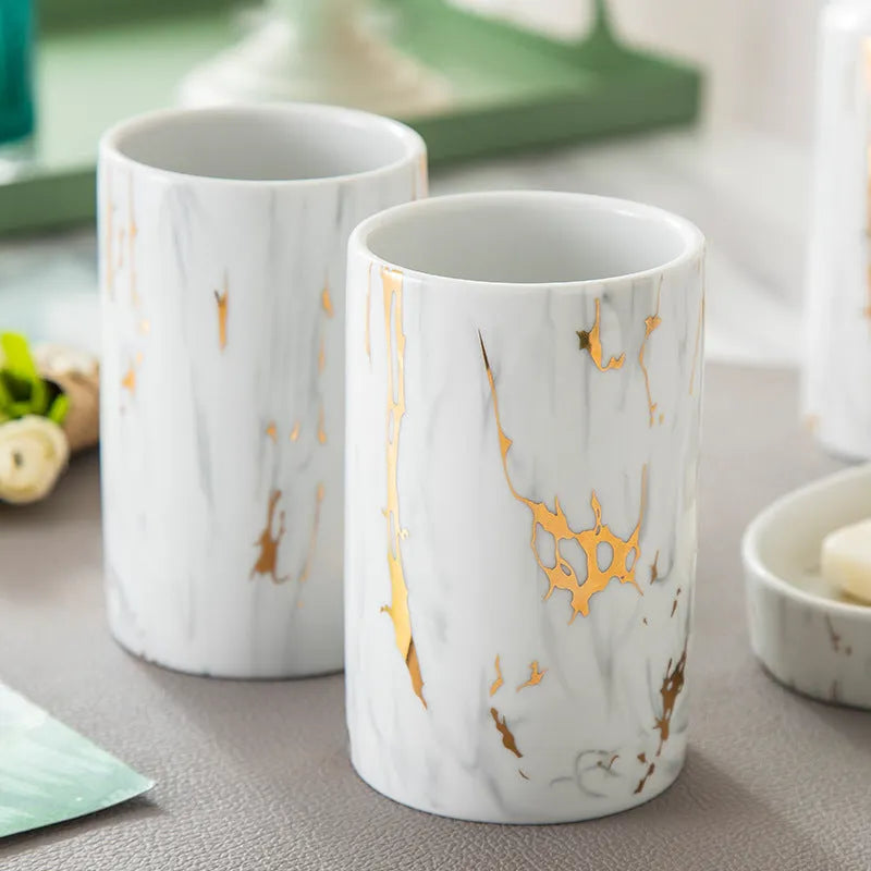 White ceramic bathroom wash kit set with two cups, a soap dish, and a bottle on a marble background.
