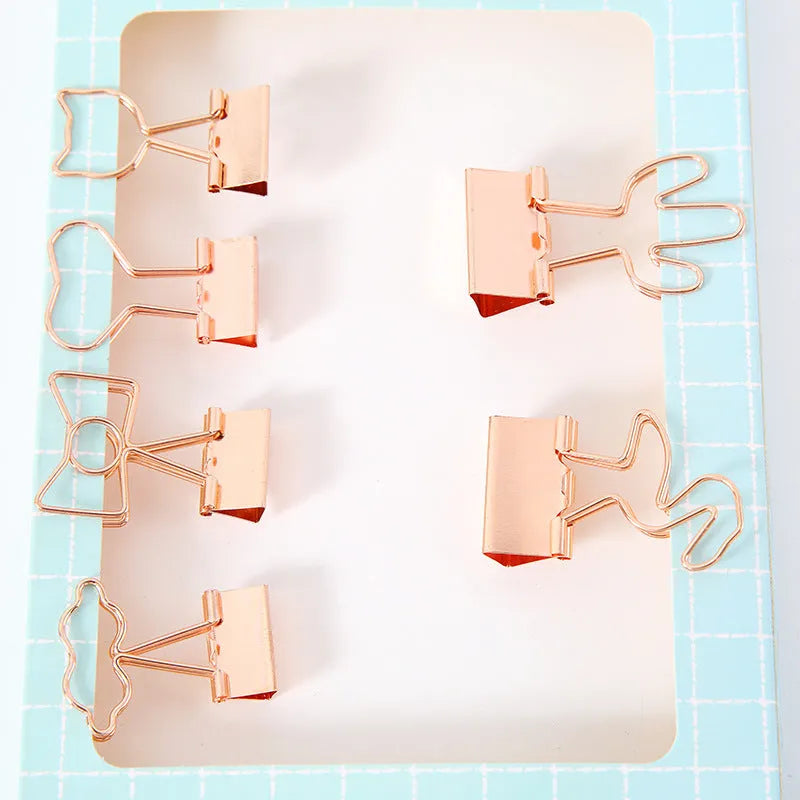 Small gold metal office clip with a long tail, shown in flamingo, love, cloud, cat, cactus, and bow shapes.