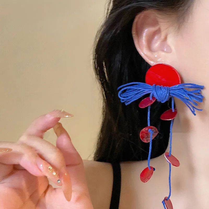 A pair of geometric cloth earrings with a blue resin flower decoration and silver needle detail.