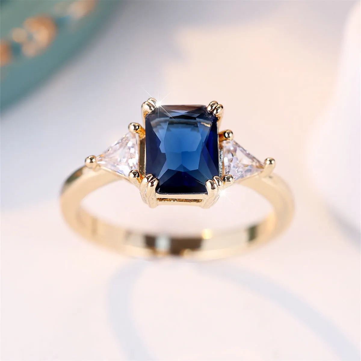 Gold and sapphire blue rectangular copper ring for women on a plain background.